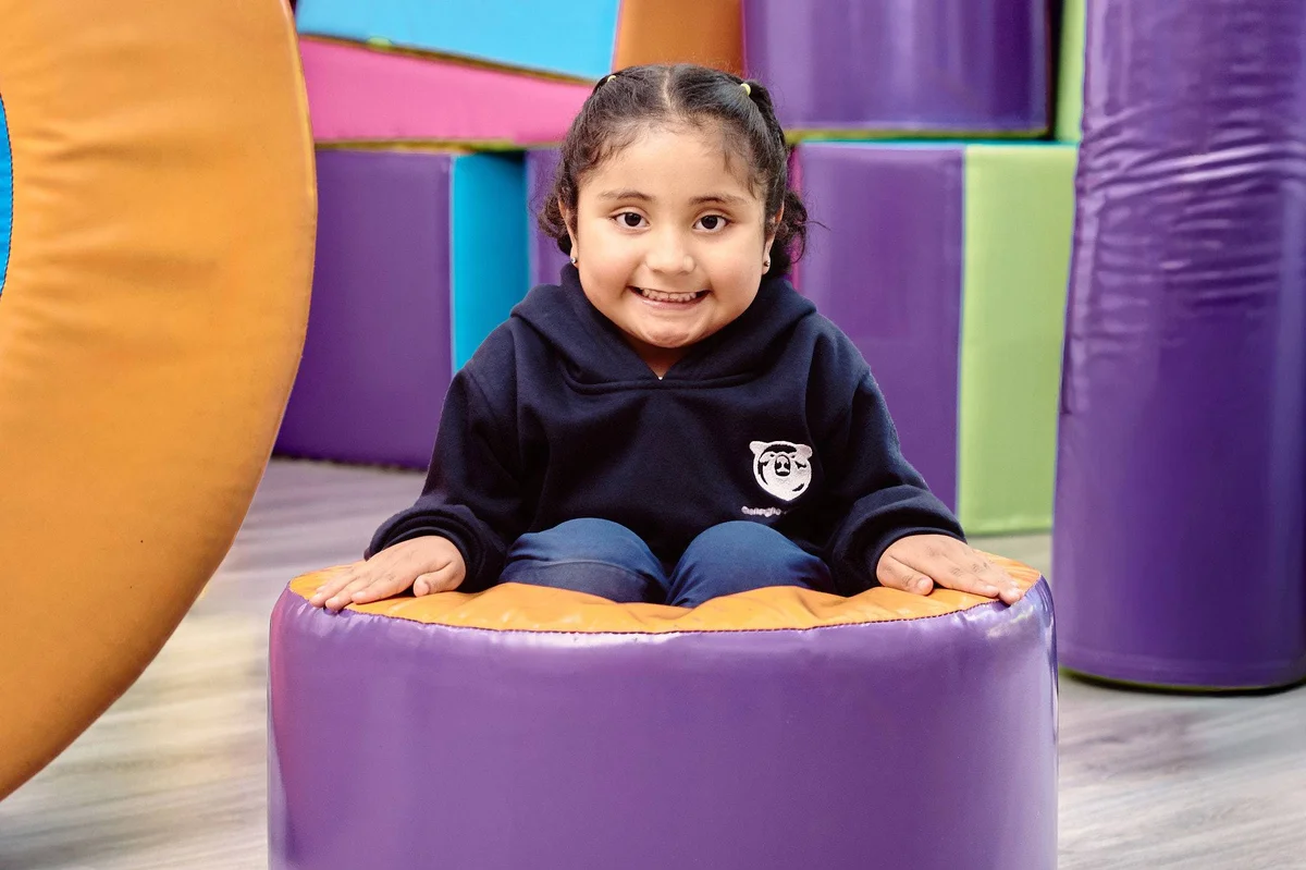 Young student smiling while sitting on colorful soft play equipment in the school's indoor play area